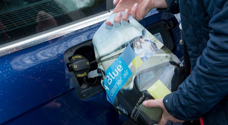 Person refilling a car with a container of Blue diesel exhaust fluid.